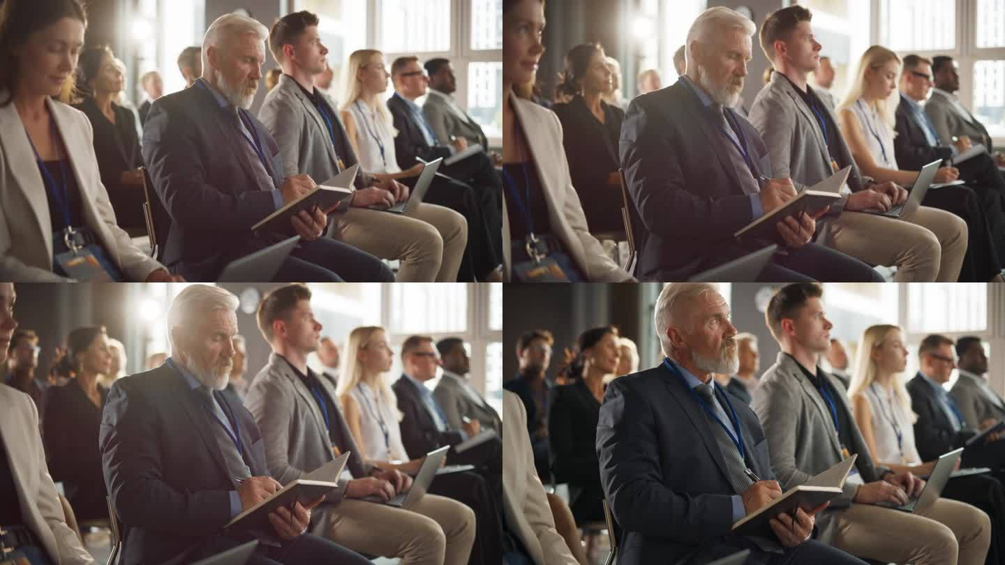 在商业论坛上，一位年长的白人男子坐在拥挤的听众中。公司代表做笔记。成功的男性CEO参加商务会议，聆听
