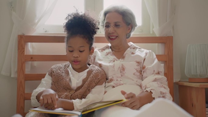 奶奶和孙女在一起看相册。奶奶在家里睡觉前给她的小孙女讲旧的回忆和故事。家庭护理