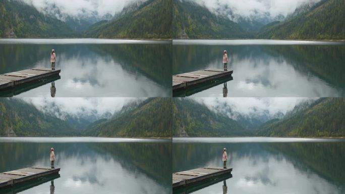 一个女人站在湖边的码头上，看着岣梢湖和山脉的景色