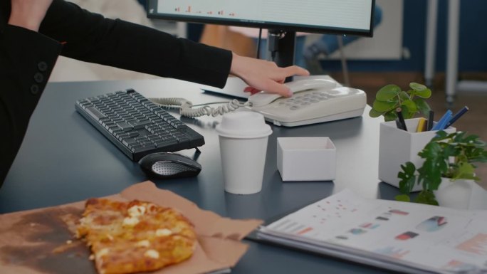 女商人坐在电脑前吃披萨片的特写