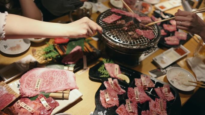 一名年轻的亚洲女子在一家餐馆里吃着传统的日式牛肉烧烤“Yakiniku”，并把生牛肉片放在木炭烤炉上