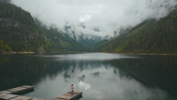 一个女人站在湖边的码头上，看着岣梢湖和山脉的景色