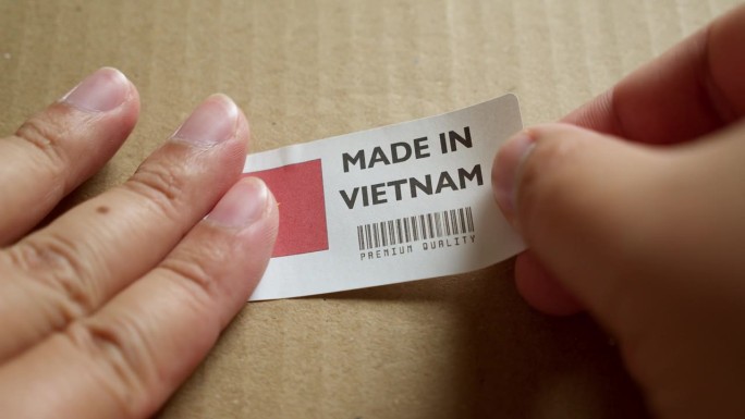 手将“越南制造”国旗标签贴在带有产品优质条形码的运输箱上。制造和交付。产品出厂进出口。