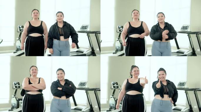 两个胖乎乎的亚洲女人穿着运动服，在健身房竖起大拇指，开心地微笑着，双臂交叉，看着对方。女人运动后的幸
