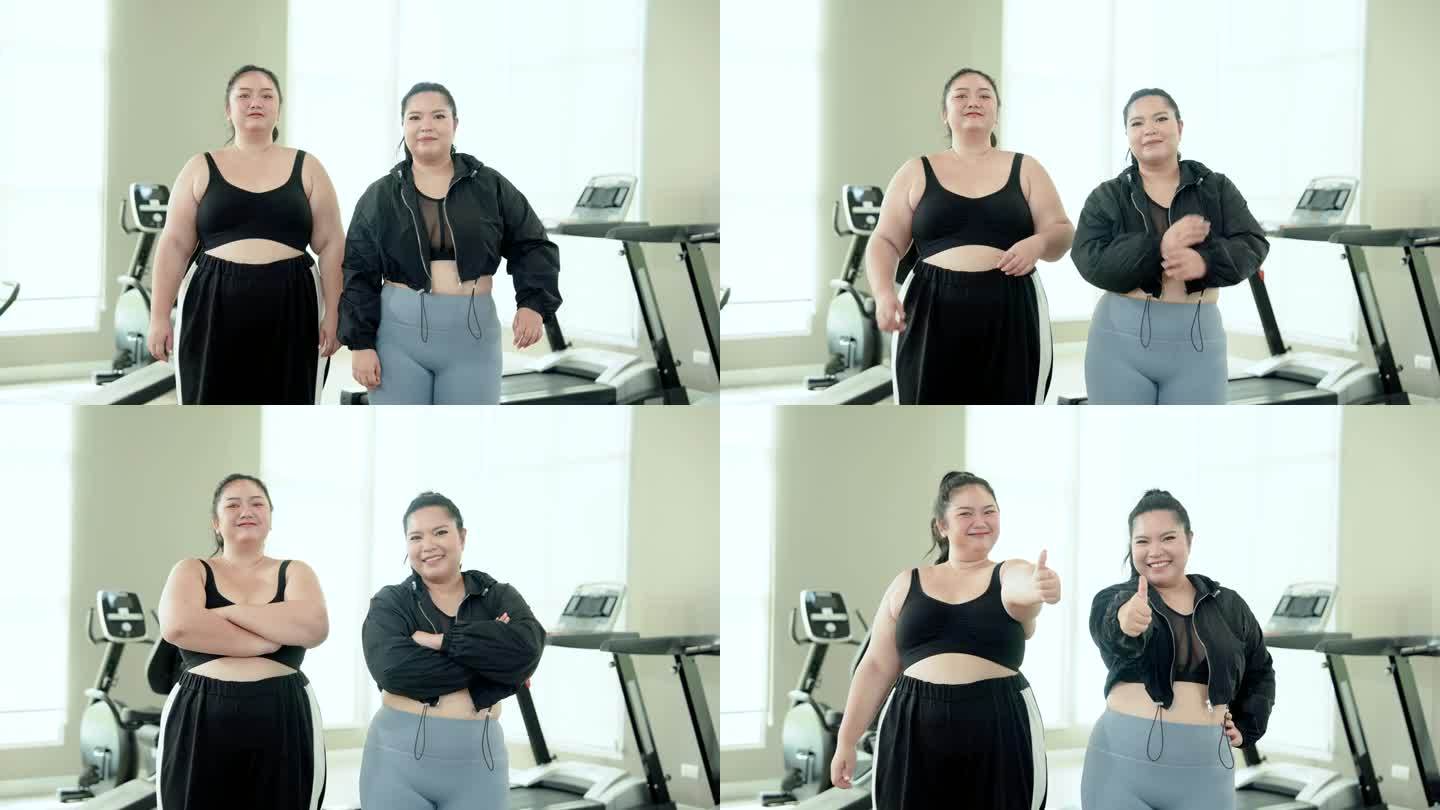 两个胖乎乎的亚洲女人穿着运动服，在健身房竖起大拇指，开心地微笑着，双臂交叉，看着对方。女人运动后的幸