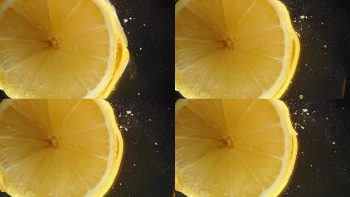 玻璃桌子上柠檬片的底部，蜂蜜滴下来，特写在黑色背景下。