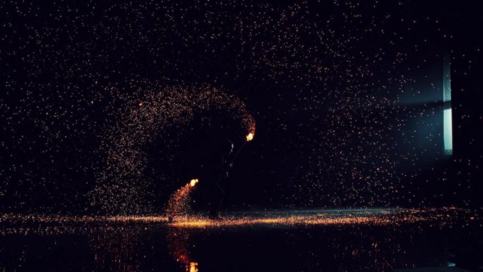 火焰艺术家在黑暗空间中旋转火球的剪影。明亮炽热的火花在房间里飞来飞去。电影超级慢动作镜头与戏剧性的速