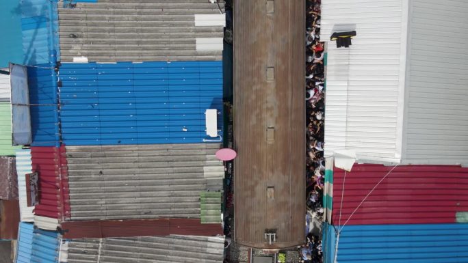 从空中俯瞰:火车抵达泰国美隆铁路市场。游客们危险地挤在铁轨旁。