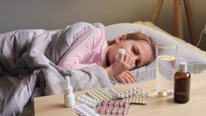 医疗疾病。孩子的健康。寒冷的安慰。健康的恢复。生病的小女孩躺在床上，拿着餐巾咳嗽，有高烧和感冒的症状