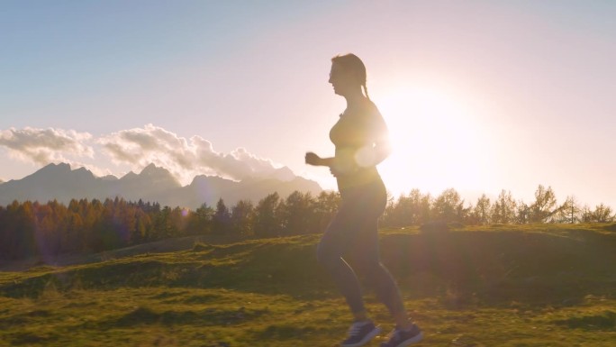 特写，镜头光晕:女性跑步者在夕阳下沿着风景优美的小路慢跑