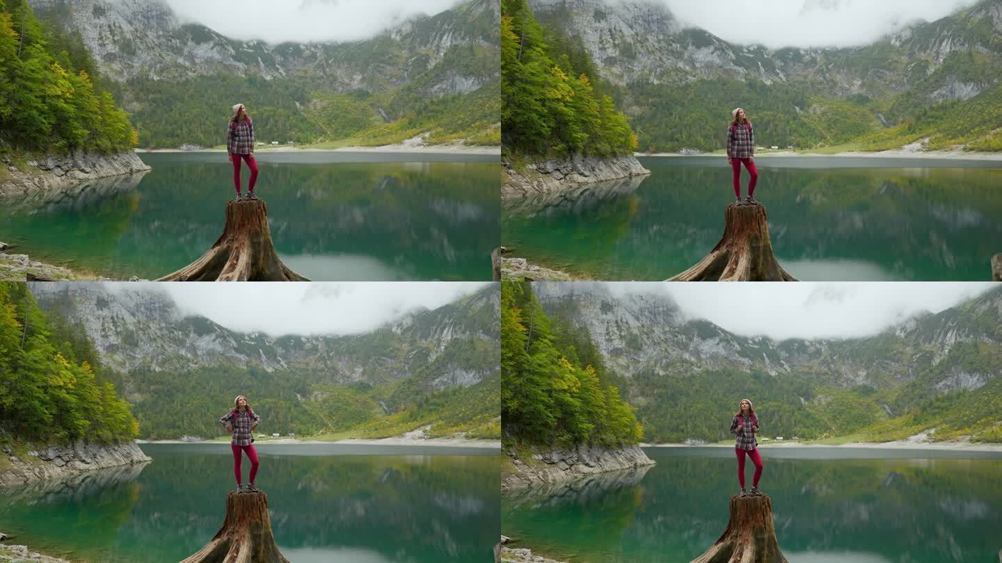女子站在山湖背景的树桩上