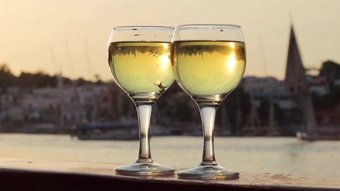 两杯白葡萄酒，以河景和船只为背景
