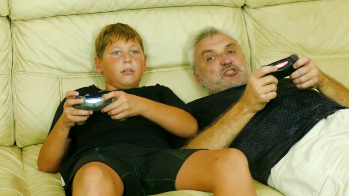 父子俩在家里的沙发上兴奋而不诚实地玩着电脑游戏