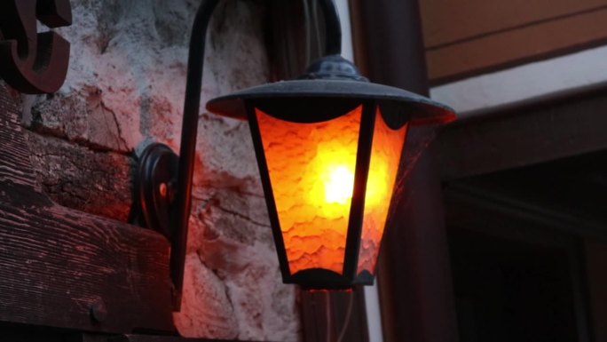 中世纪的石墙上挂着一盏旧式图案的金属灯笼，里面有火焰。它投射出一种温暖的橙色光，与复古和乡村风格的深
