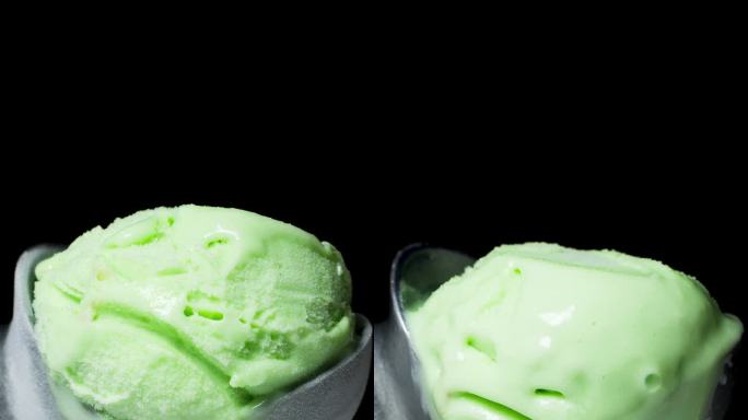 垂直视频。黑色背景下，开心果绿色的冰淇淋球在特制的金属勺子上迅速融化。