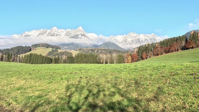 秋天的景色，翠绿的农家田野映衬着明亮的蓝天和白雪覆盖的高山，奥地利