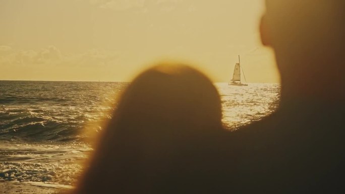 冲浪夫妇带着冲浪板在日落的海洋上看帆船