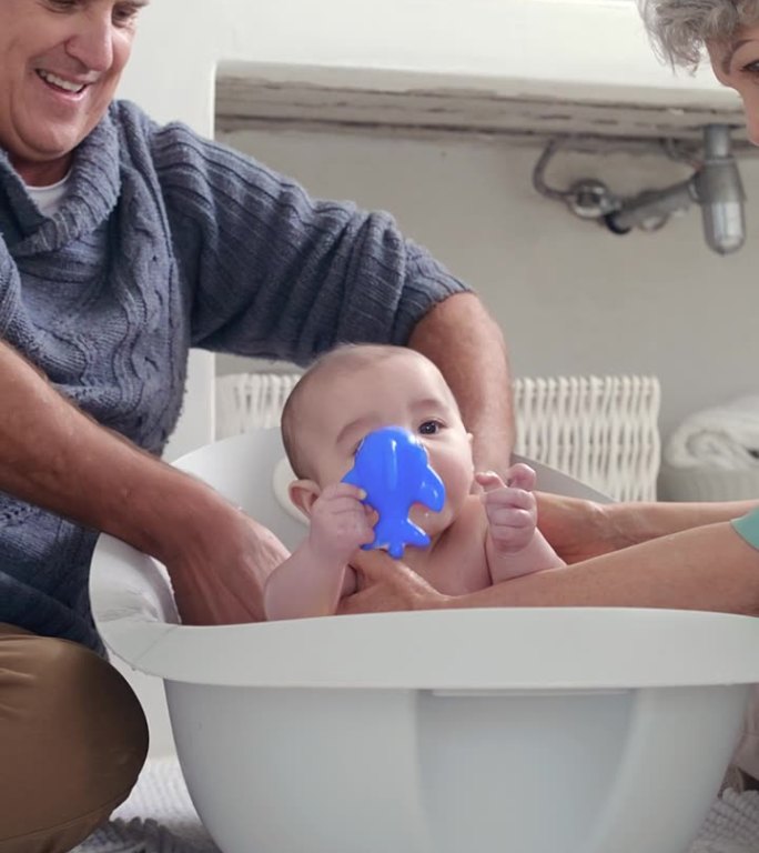 奶奶、爷爷和婴儿在浴室地板上洗澡，以保持卫生或照顾孩子。家庭，孩子和年长的祖父母或在房子里用水清洗新