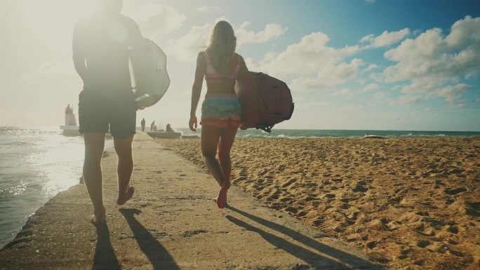 冲浪夫妇在阳光明媚的海滩上带着冲浪板散步