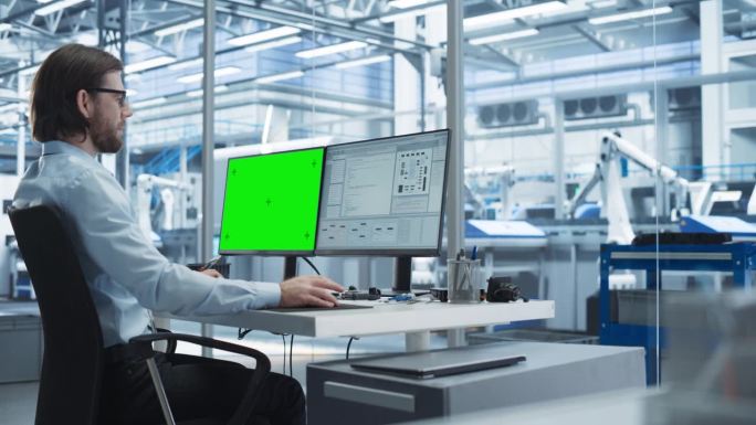 年轻的软件开发人员在工厂办公室里使用绿屏Chromakey模拟显示器的台式电脑工作。技术研发工厂，配