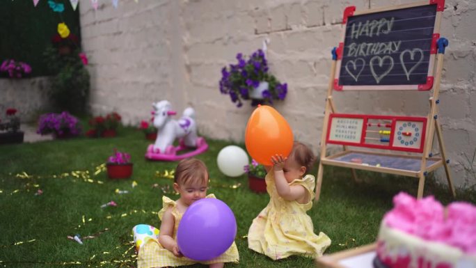 一对双胞胎姐妹在后院一起玩气球庆祝她们的一岁生日
