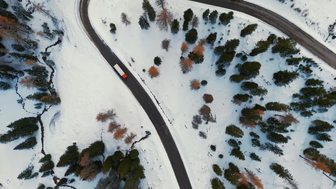 无人机拍摄的卡车行驶在雪山蜿蜒的道路，白云石