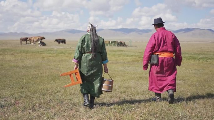 一对蒙古夫妇扛着桶穿过牧场去挤牛奶