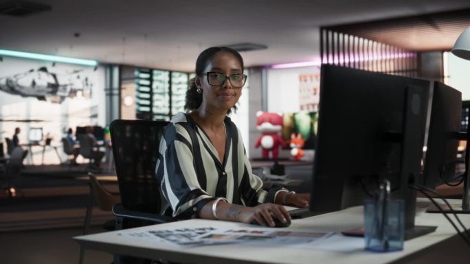 成功的黑人女商人使用台式电脑，分析数据，思考和解决问题的肖像。创意公司现代办公室里微笑着看镜头的女经
