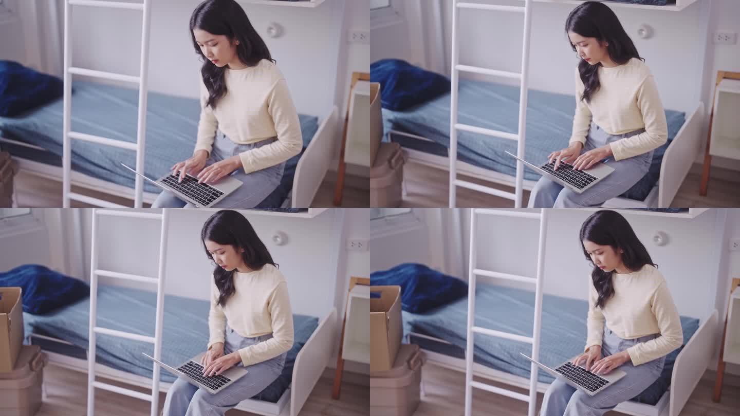 穿着便服的亚洲女学生在宿舍的双层床上用笔记本电脑写作业或写研究项目或论文。