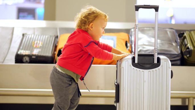 坚定的小男孩推着小手提箱通过机场行李认领大厅