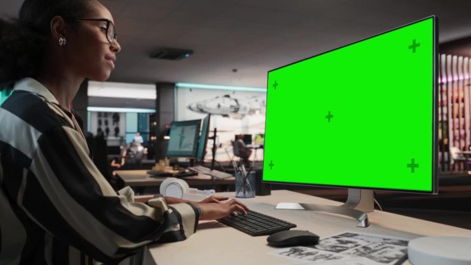 创意黑人女性使用桌面电脑与模拟绿屏Chromakey。在游戏开发公司工作的女性视觉特效艺术家，为冒险
