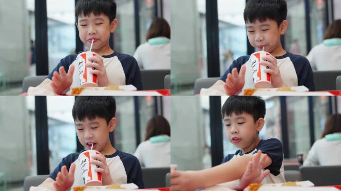 亚洲男孩在热闹的快餐店的快乐用餐体验。孩子坐在一张光线充足的桌子旁，脸上挂着欢快的微笑，津津有味地品