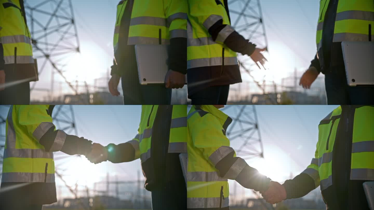 图为身穿反光外套的工程师在明亮的电站里握手。在电影般的慢镜头中，穿着反光外套的工程师们在阳光灿烂的发