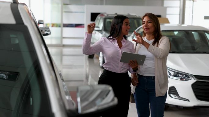 快乐的销售人员向一位有兴趣买车的女士展示一辆车