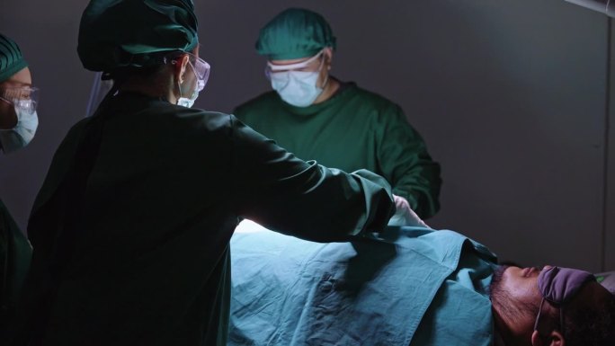 一个装有各种手术工具和医疗用品的医疗托盘的特写，一名护士在手术室手术前用绿布盖住躺在手术床上的昏迷病