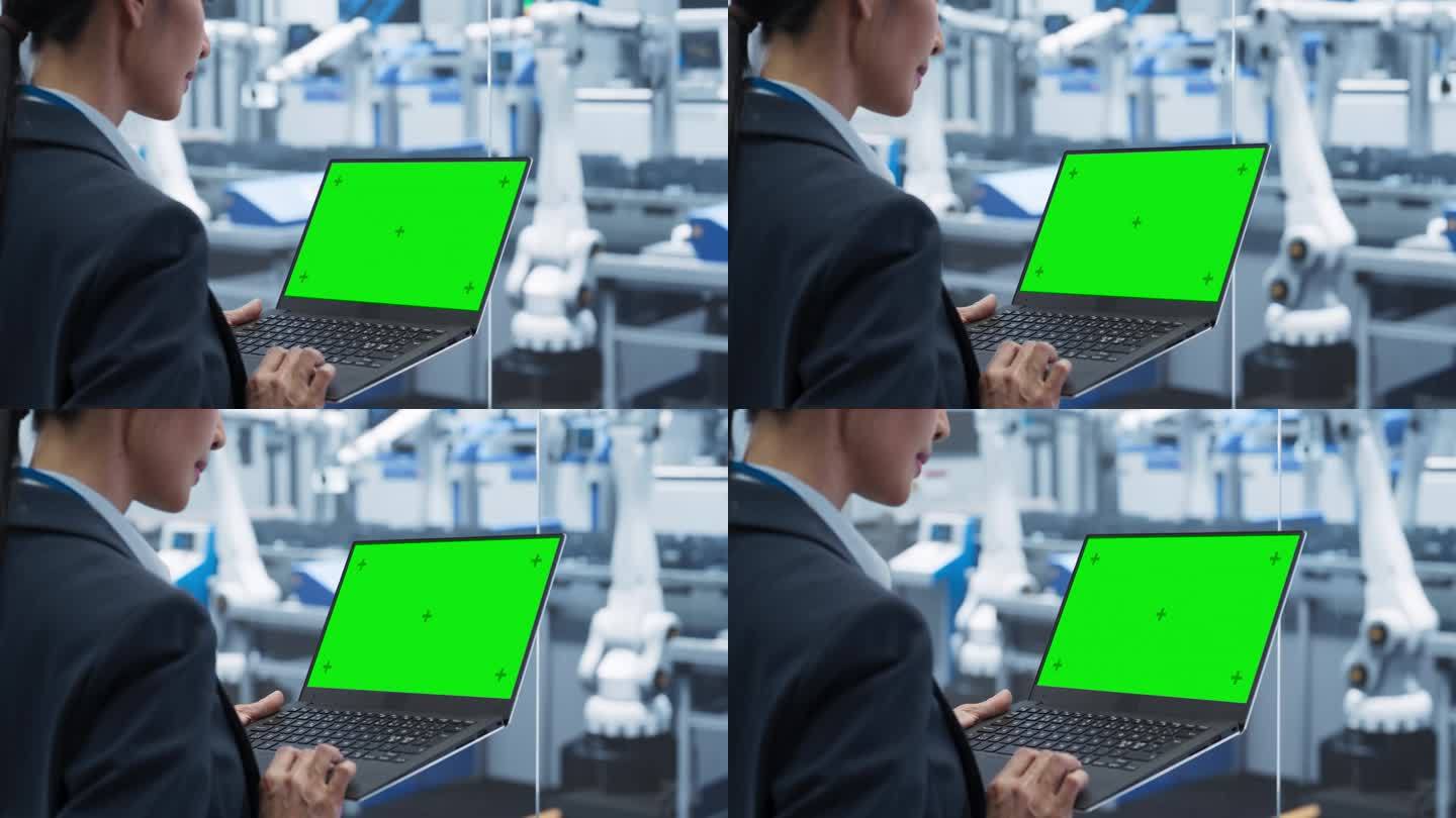 亚洲女工程师使用绿屏模拟显示的笔记本电脑。一位年轻的妇女在工厂里用现代电子机器监督生产。过肩投篮
