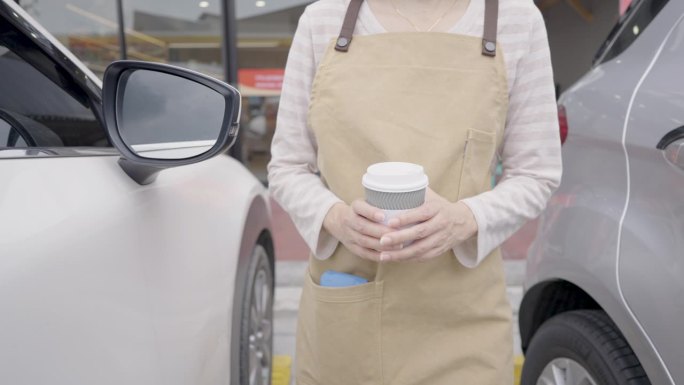 亚洲女服务员走到车里给顾客送咖啡。通过开车或开车过街的方式买一份外卖或咖啡。