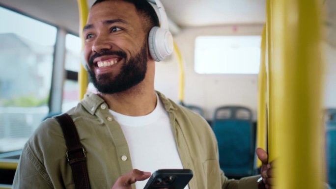一名男子在公交车上带着手机和耳机，微笑着在城市通勤，快乐地开车。公共交通，服务或乘车，在智能手机上听
