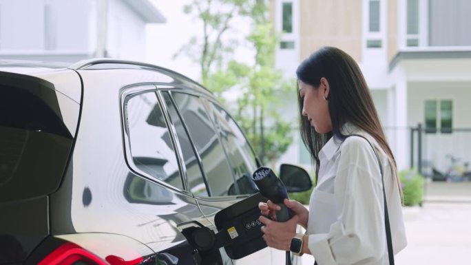 一名妇女将电源插入正在充电的电动汽车。