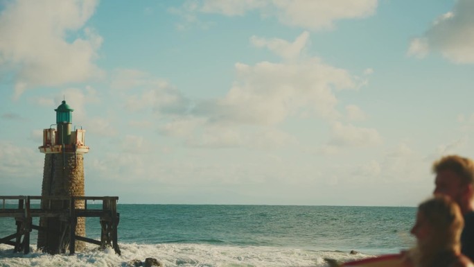 一对冲浪夫妇在有灯塔的阳光海滩上玩冲浪板