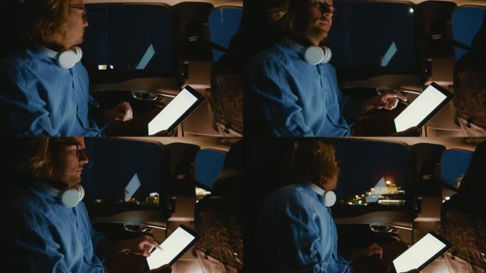 一名男子晚上在汽车后座上戴着耳机使用数码平板电脑