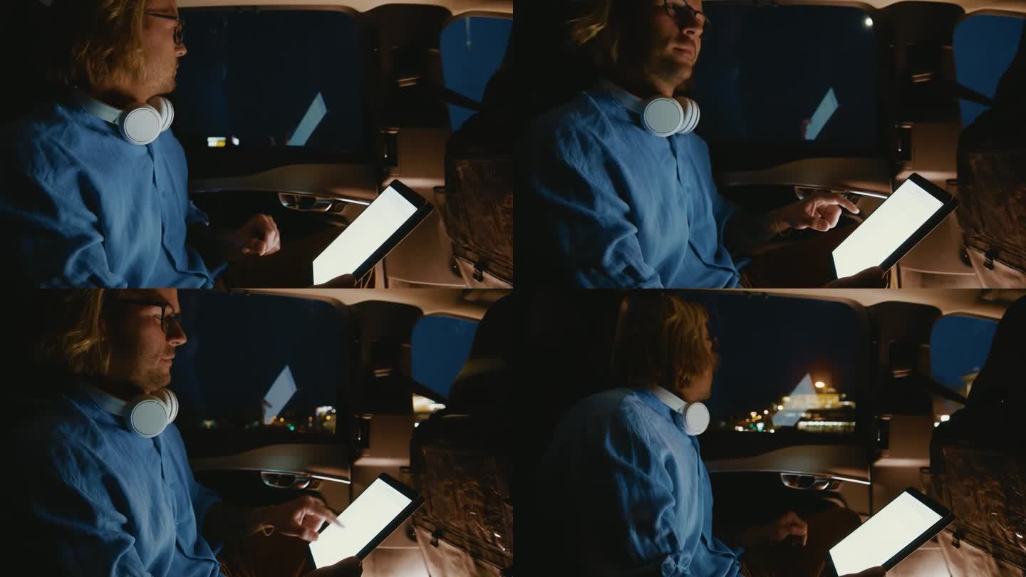 一名男子晚上在汽车后座上戴着耳机使用数码平板电脑