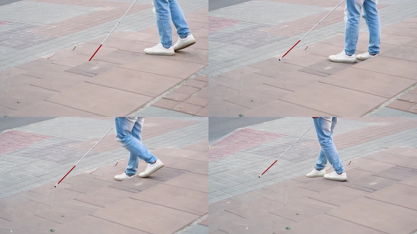 手持白色手杖的盲人青年在城市中穿过街道的中间部分。近距离的腿和手杖