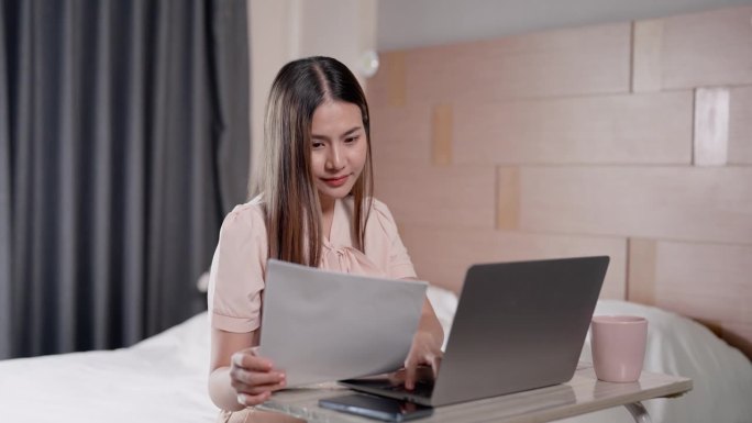 是时候在家工作了，漂亮的亚洲长发女人坐在卧室床上的笔记本电脑前打文件准备节假日给主管发会议纪要。