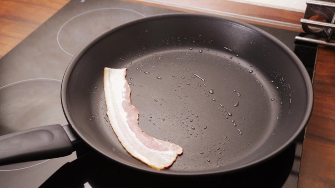 煎腊肉，女手把腊肉片放在煎锅上，煮英式早餐