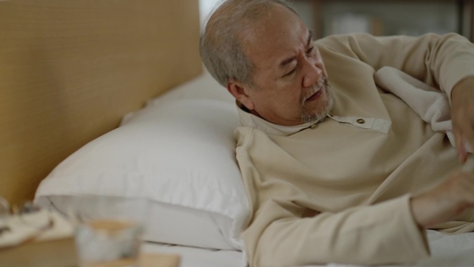 亚洲老人睡觉时咳嗽，醒来后喝水。