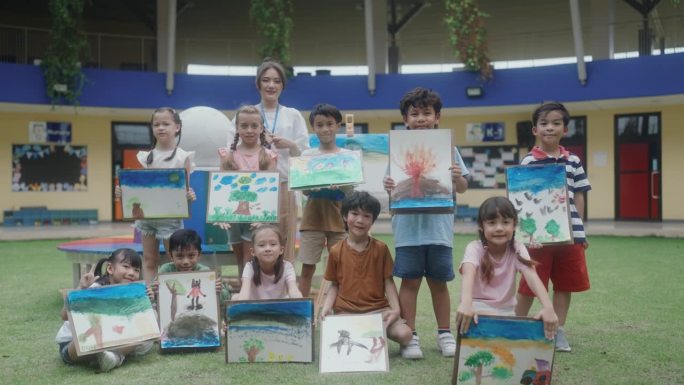 小学生在课堂美术展览中展示多彩的水彩画。年轻女老师骄傲地带领学生在学校的水彩艺术课展示。