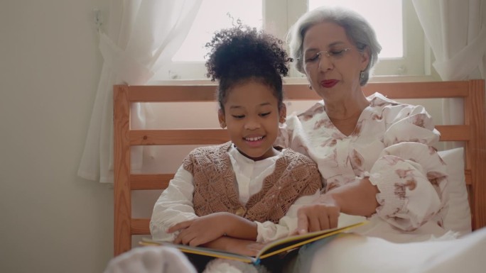 美丽、优雅的非裔美国老年祖母和她的小孙女坐在家里的卧室里，看着家庭相册里的照片。与家人共度时光。家庭