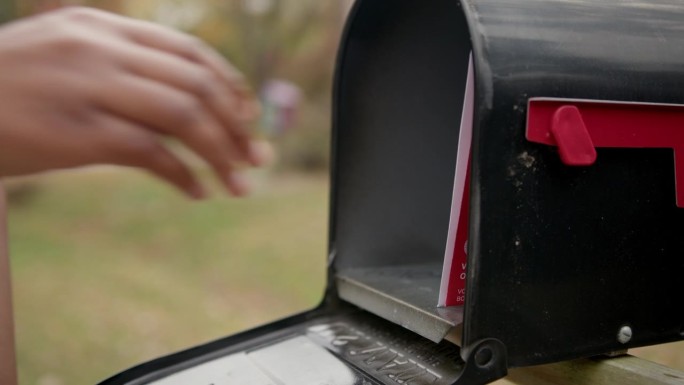 一名黑人妇女在郊区的邮箱前接收邮寄选票，以便在美国总统、参议院、国会或地方选举中投票