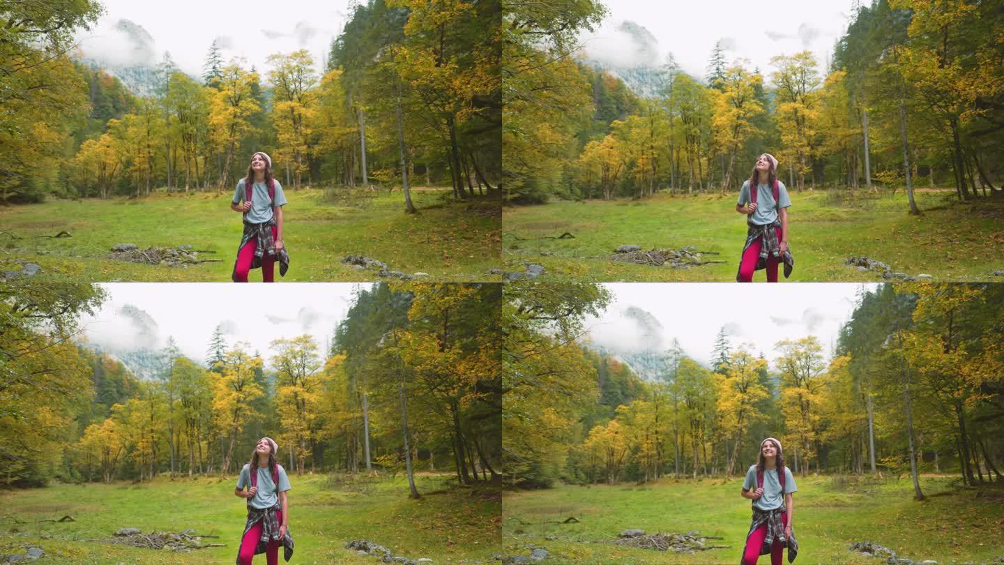 快乐的女人在秋天的森林里徒步旅行，敬畏地看着风景